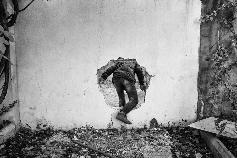 A member of Civilian Protection Unit (YPS) uses a hole in a wall to cross a street controlled by Turkish special military forces, Nusaybin, Turkey,  December 2015, © Emin Ozmen/Magnum Photos 